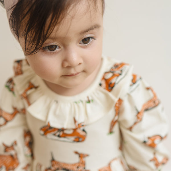 A child wearing a cream-colored dress with a fawn allover print, featuring a frill collar and slightly puffed sleeves. by fauna.ie