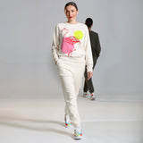 A female model wearing a beige tracksuit with a flamingo illustration on the chest area, by fauna.ie