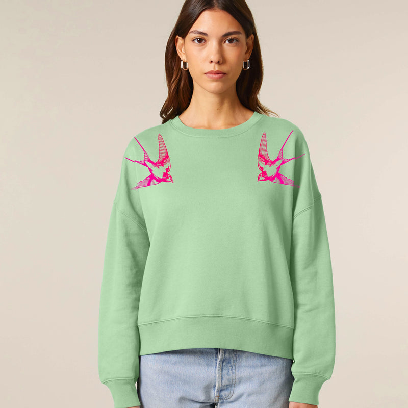 Person wearing a light green sweatshirt with pink swallows by fauna.ie