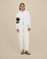 Person wearing a white shirt with a bee design and white pants on a beige background